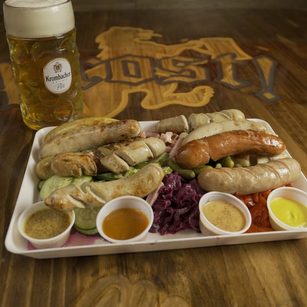 A platter of various sausages, red cabbage, pickles, and sauces, with a beer stein.