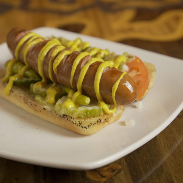 Grilled hot dog with mustard, pickles, and tomato on a poppy seed bun.