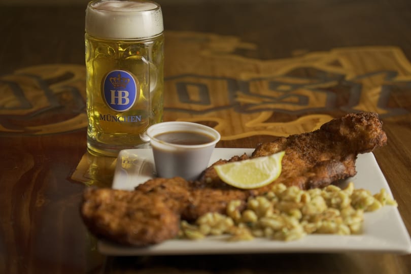 Crispy fried fish with spaetzle, a lemon wedge, and a mug of Hofbräu München beer.