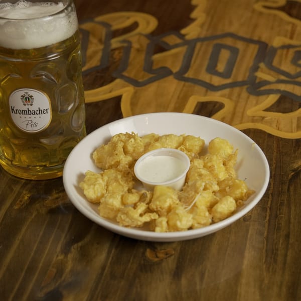 A glass of Krombacher Pils beer and a plate of fried cheese curds with ranch dressing.